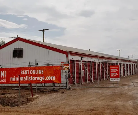 Outdoor drive-up self-storage facility with white buildings, red trim, and a chain-link security gate turn-around