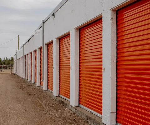 Row of drive-up self-storage units with orange roll-up doors and a white exterior wall