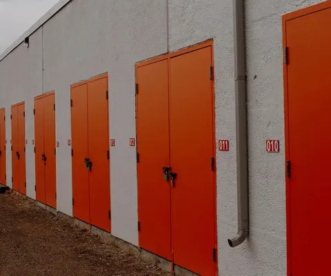 A row of outdoor self-storage units with bright orange doors and red unit number signs outdoors