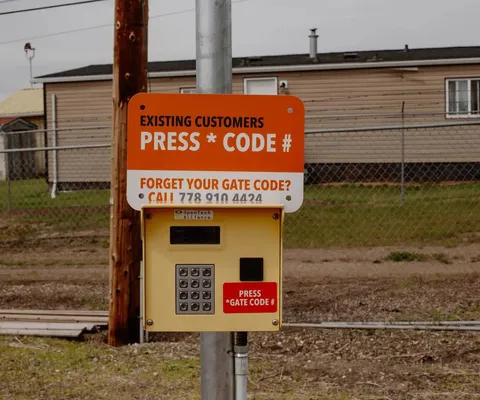 An electronic gate keypad with instructions for existing customers to enter their gate code under an orange sign