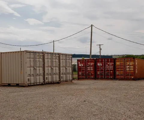 Outdoor gravel storage lot featuring rows of tan and red metal shipping containers under power lines