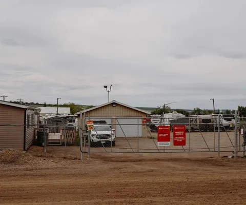 A chain-link gate with red signage provides access to a gravel storage lot for vehicles and RVs