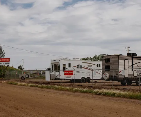 Outdoor RV and boat storage lot with campers parked behind a chain-link fence and red signage