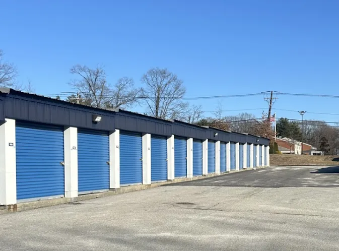Drive-up self-storage units in Providence, RI, with blue roll-up doors alongside a wide asphalt driveway under clear skies