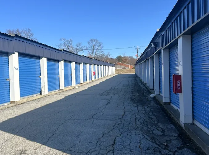 Long rows of outdoor drive-up storage units in Providence, RI, with blue roll-up doors and white trim under a sunny sky
