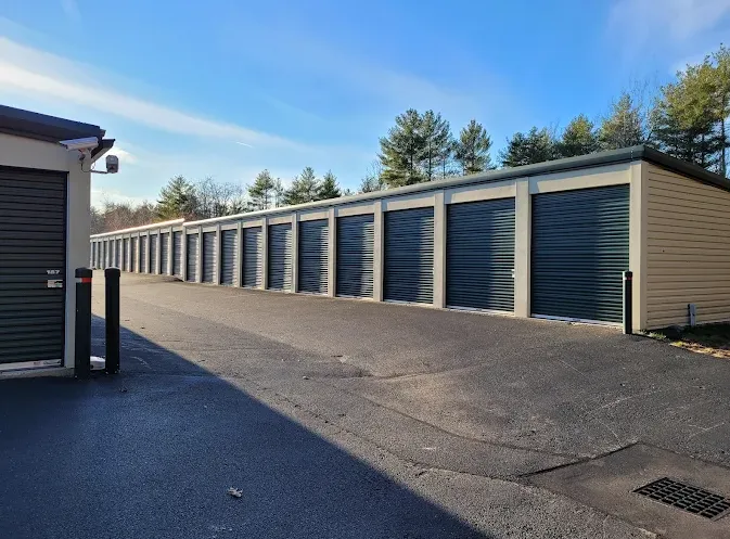 A long row of outdoor drive-up storage units with dark green roll-up doors and asphalt driveway
