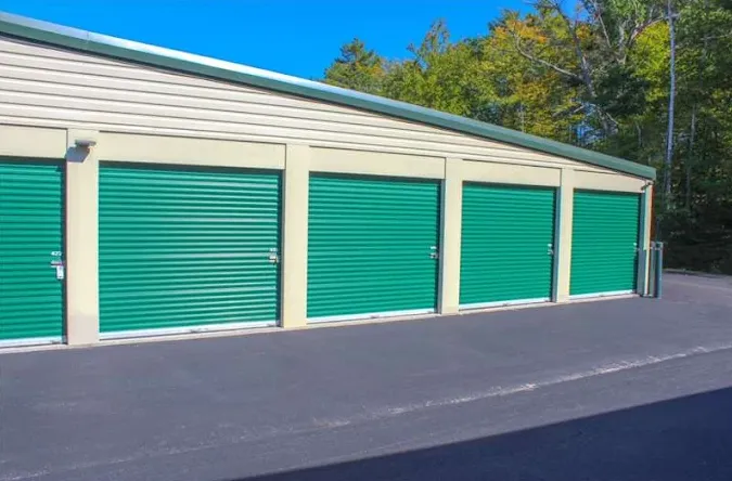Exterior view of drive-up self-storage units in Cape Neddick with green roll-up doors and a paved driveway