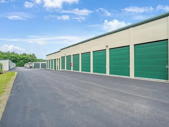 Exterior of a storage building featuring several green roll-up unit doors and a paved driveway