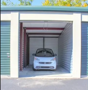 Small white car parked inside an open drive-up self-storage unit with corrugated metal walls