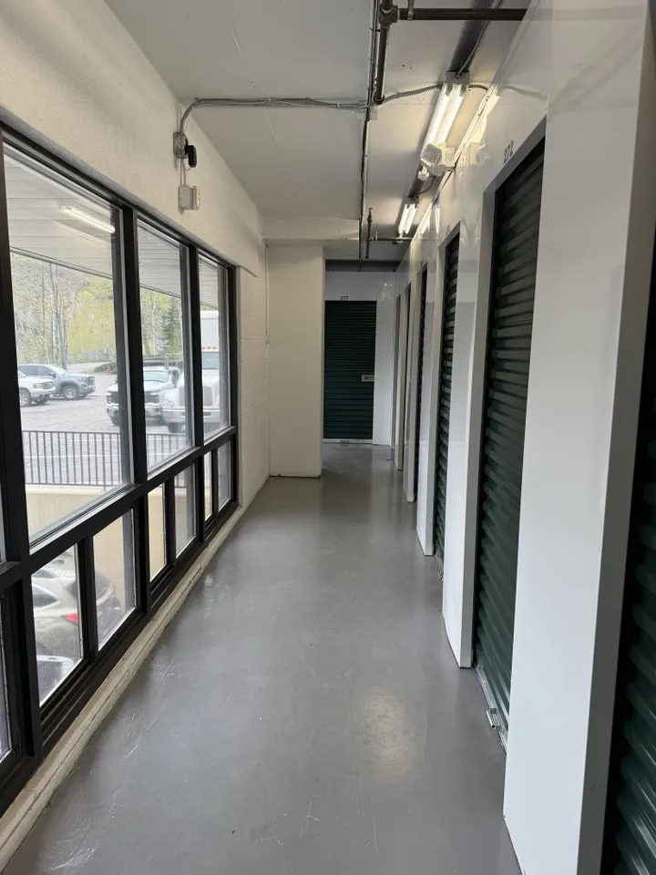 Upper-floor hallway with indoor climate-controlled storage units in Avon at 910 Nottingham Road, with green roll-up doors opposite a wall of windows