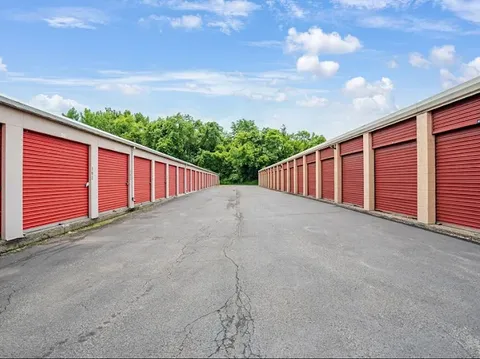 Rows of drive-up storage units in Cohoes at 50 Oliver St, with red roll-up doors along wide paved aisles and green trees