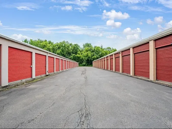 Rows of drive-up storage units in Cohoes at 50 Oliver St, with red roll-up doors along wide paved aisles and green trees
