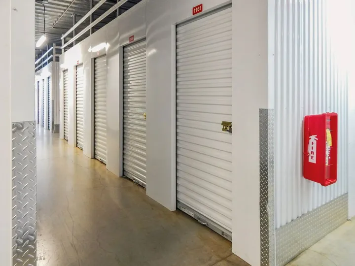 A bright hallway of indoor climate-controlled storage in North Augusta on Cork Tree Bend, featuring white roll-up unit doors and a red fire extinguisher cabinet