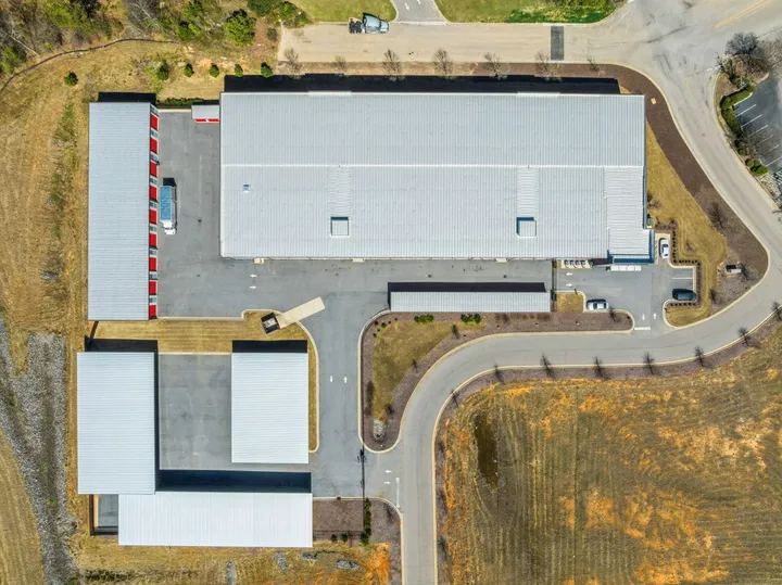 Aerial top-down view of self-storage buildings with white metal roofs, paved driveways, and red drive-up units in North Augusta on Cork Tree Bend