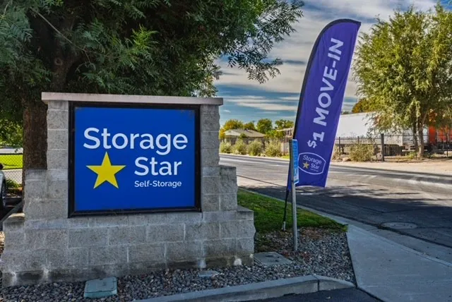 A blue Storage Star Self-Storage monument sign stands near a blue feather flag on the corner of the Woodland Storage Star driveway and Matmor Rd