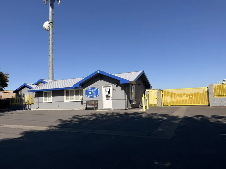 Leasing office at Storage Star Self-Storage in Woodland, CA, with grey siding, blue trim, and a yellow gated entry under a clear sky