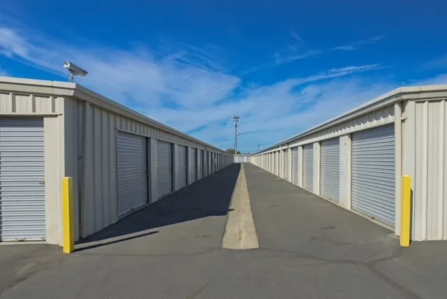 Drive-up self-storage units in Woodland on Matmor Rd with gray roll-up doors line both sides of a paved drive aisle