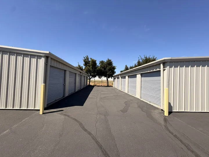 Outdoor drive-up storage units on Matmor Rd with gray roll-up doors and a wide asphalt driveway under a clear blue sky