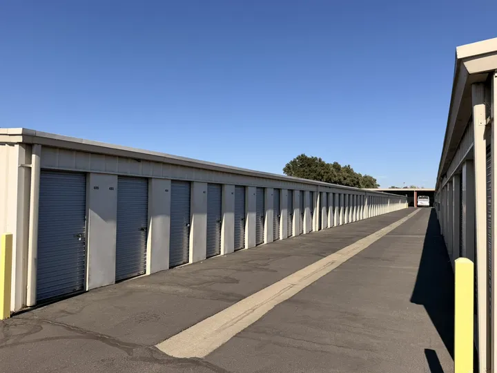 Outdoor drive-up storage units in Woodland on Matmor Rd with gray roll-up doors and an asphalt driveway under a clear blue sky