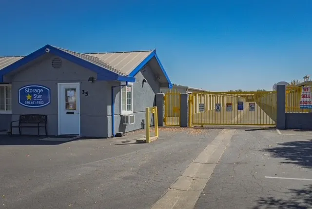 An outdoor keypad entry and yellow metal gate next to a gray office at Storage Star Self-Storage on Matmor Rd