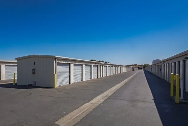 An asphalt driveway runs between long rows of outdoor drive-up storage units in Woodland, CA, with gray roll-up doors