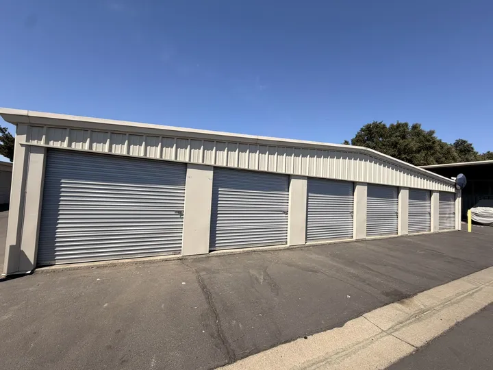A row of drive-up self-storage units in Woodland, CA, with gray roll-up doors along a paved asphalt driveway
