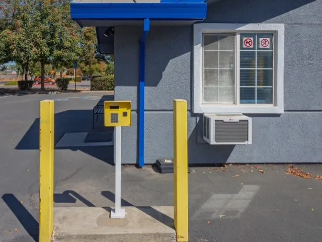 Yellow keypad entry stands between two yellow bollards outside a gray Storage Star building on Matmor Rd