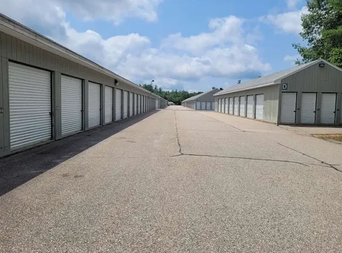 Rows of drive-up self-storage units in Somersworth, NH, with white roll-up doors along a paved asphalt driveway