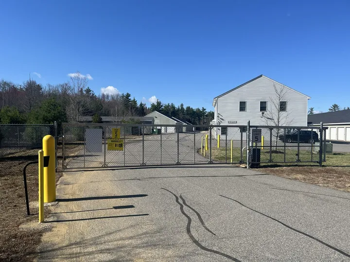 A sliding chain-link security gate at a self-storage facility in Somersworth, NH, next to a white office building