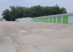A row of drive-up self-storage units with green roll-up doors and wide drive aisles