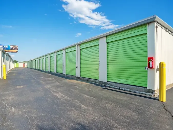 Row of outdoor drive-up storage units in Albany on Central Ave with bright green roll-up doors along an asphalt driveway under a blue sky