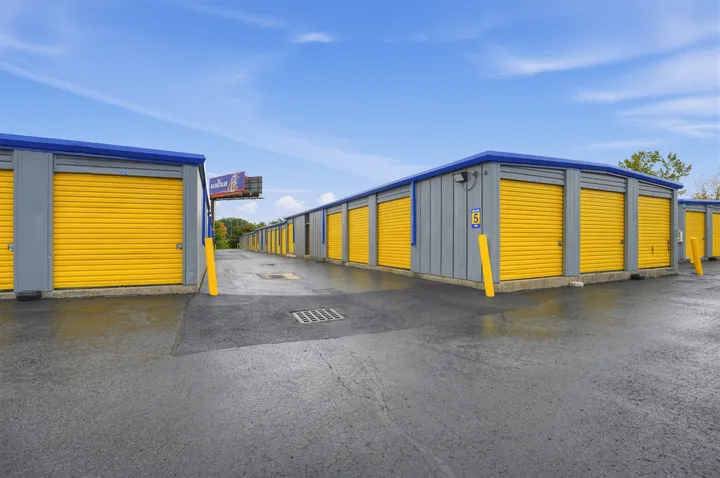 Rows of gray drive-up storage units in Albany with yellow roll-up doors and blue trim along an asphalt driveway