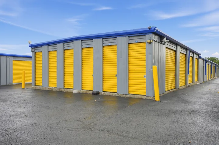 Outdoor drive-up self-storage units in Albany, NY, with yellow roll-up doors and gray siding under a blue sky