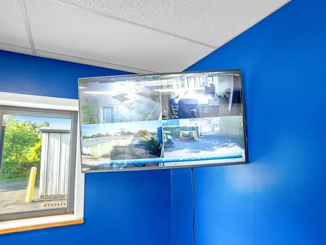 Wall-mounted security monitor displaying four camera angles of the Albany storage facility office and exterior grounds
