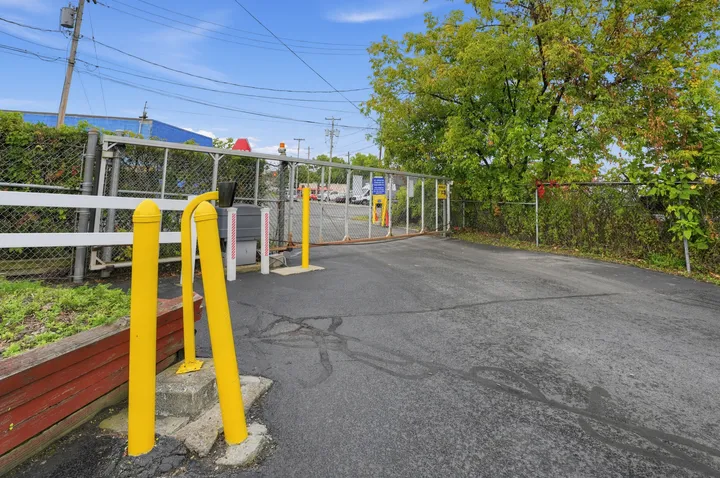 A gated asphalt entrance to Storage Star on Central Ave with yellow safety bollards and a keypad access station