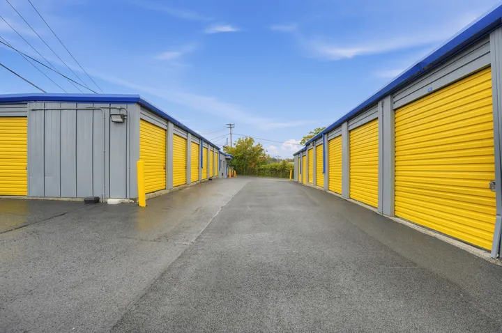 Outdoor drive-up storage units in Albany, NY, with yellow roll-up doors and gray siding along a paved alleyway
