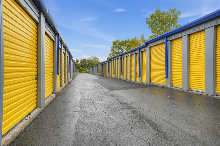 Two long rows of yellow drive-up storage units in Albany at 1025 Central Ave along an asphalt driveway under a blue sky