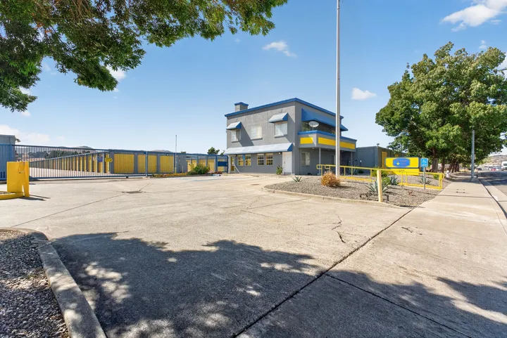 A two-story gray office building with blue trim next to a gated entrance and yellow drive-up storage units at Storage Star Self-Storage in Fairfield on Lopes Rd