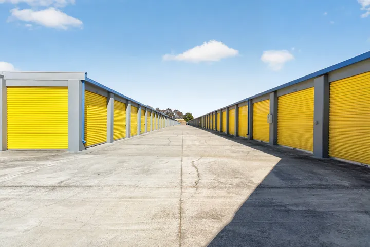 Wide concrete driving lane between long rows of yellow drive-up storage units in Fairfield on Lopes Rd under a blue sky