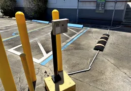 Electronic keypad entry system on a black post surrounded by yellow bollards and a speed bump