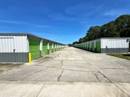 Concrete driveway between two long storage buildings with green roll-up doors under a clear blue sky