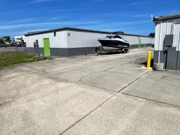 A boat on a trailer parked outside a storage building with white and gray corrugated walls