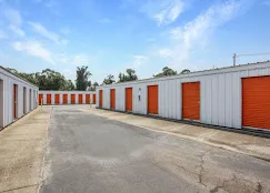 Outdoor drive-up self-storage units in Little River, SC, with white metal siding and orange roll-up doors under a blue sky