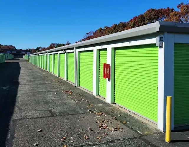 Outdoor drive-up storage units in Holtsville at 970 Waverly Ave, with bright green roll-up doors and a red fire extinguisher box
