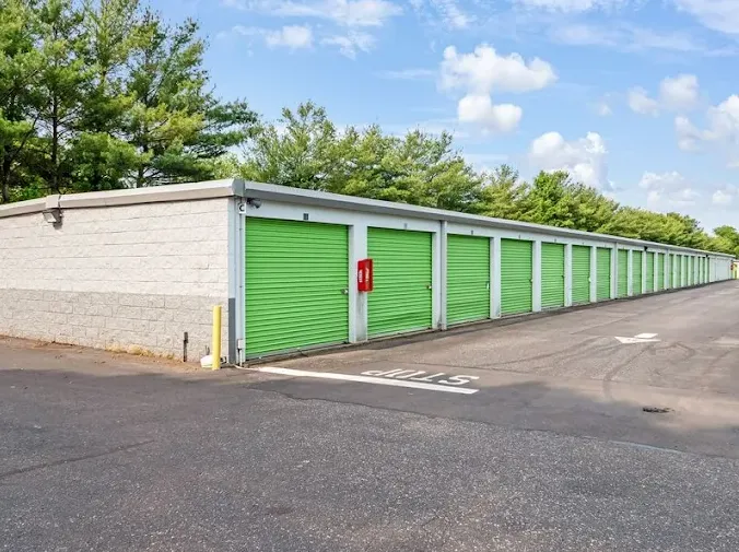 A row of drive-up self-storage units in Holtsville on Waverly Ave with green roll-up doors along a wide asphalt driveway