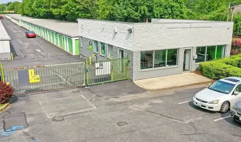 Gray stone office at Storage Star Self-Storage in Holtsville, NY, with green-doored drive-up units behind a metal security gate and paved parking lot