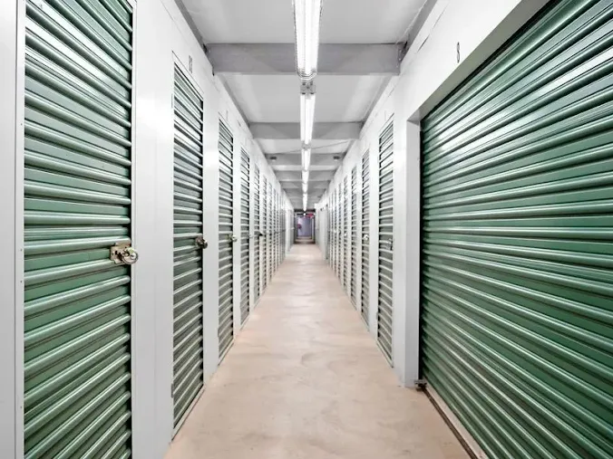 Hallway of indoor climate-controlled storage in Holtsville at 970 Waverly Ave, with green roll-up metal doors and bright overhead fluorescent lighting