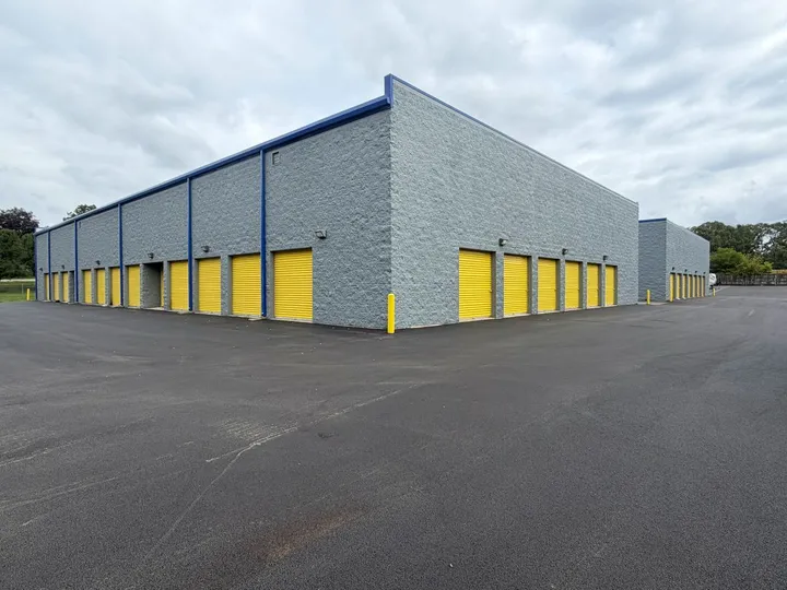 Exterior view of a gray stone storage building featuring multiple yellow drive-up units in West Chicago with wide paved driveways