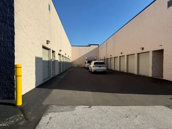 A paved driveway between storage buildings with a moving truck and white car parked by units