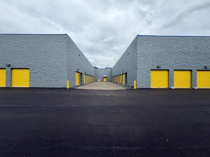 Drive-up storage units in West Chicago with yellow roll-up doors and gray walls under a cloudy sky
